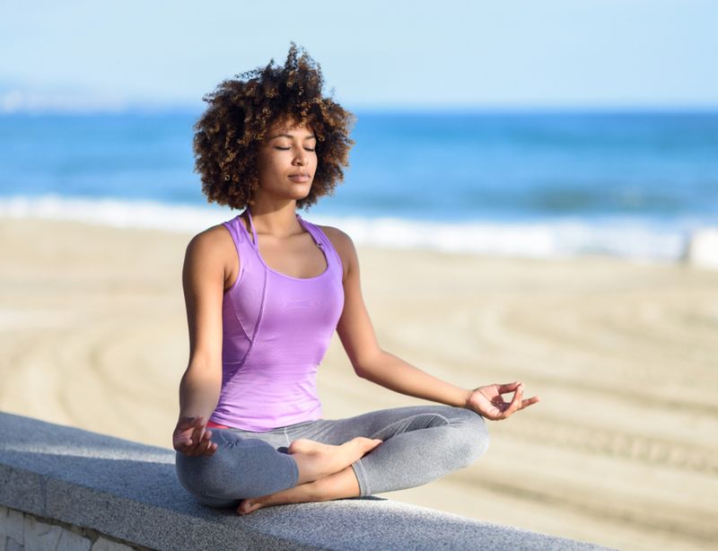 Mulher com roupa de academia medita na praia