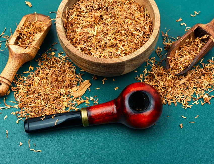 cachimbo e tabaco dispostos sobre uma superfície verde