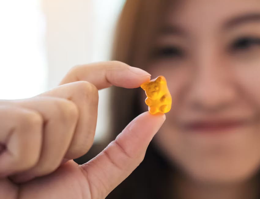 mulher segurando uma goma de thc laranja em formato de ursinho