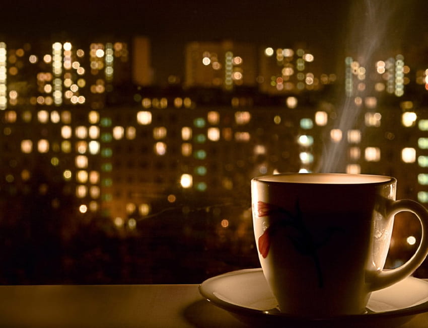 Vapor saindo de uma xícara de café fotografada em frente às luzes da cidade