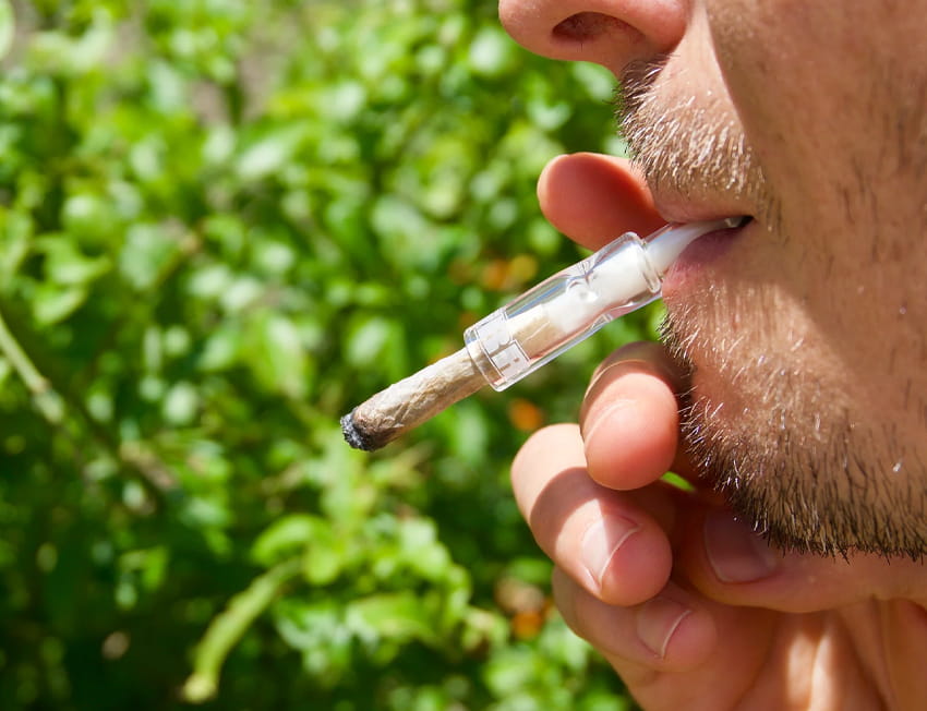 close up de pessoa fumando um baseado com piteira de vidro