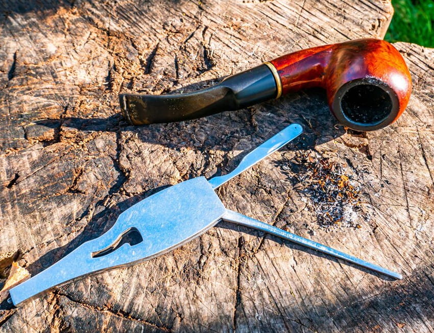 cachimbo colocado sobre um tronco de madeira com um acessório para limpeza ao lado