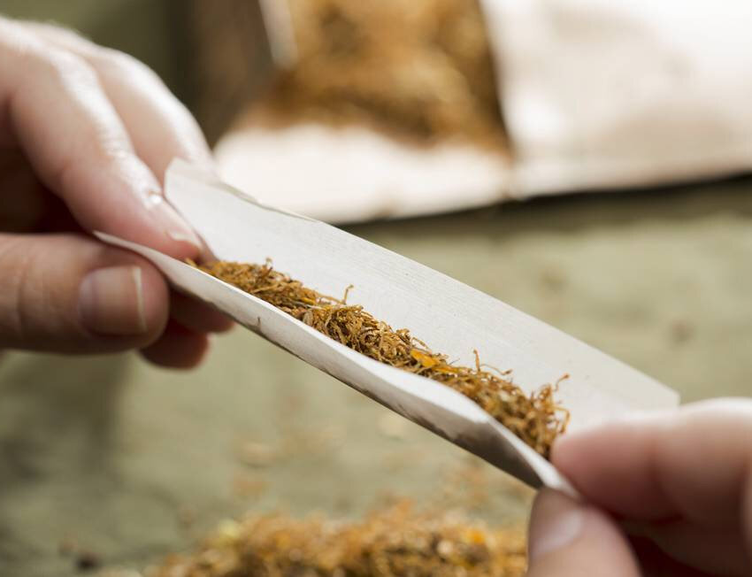 Pessoa enrolando tabaco em papel vegetal