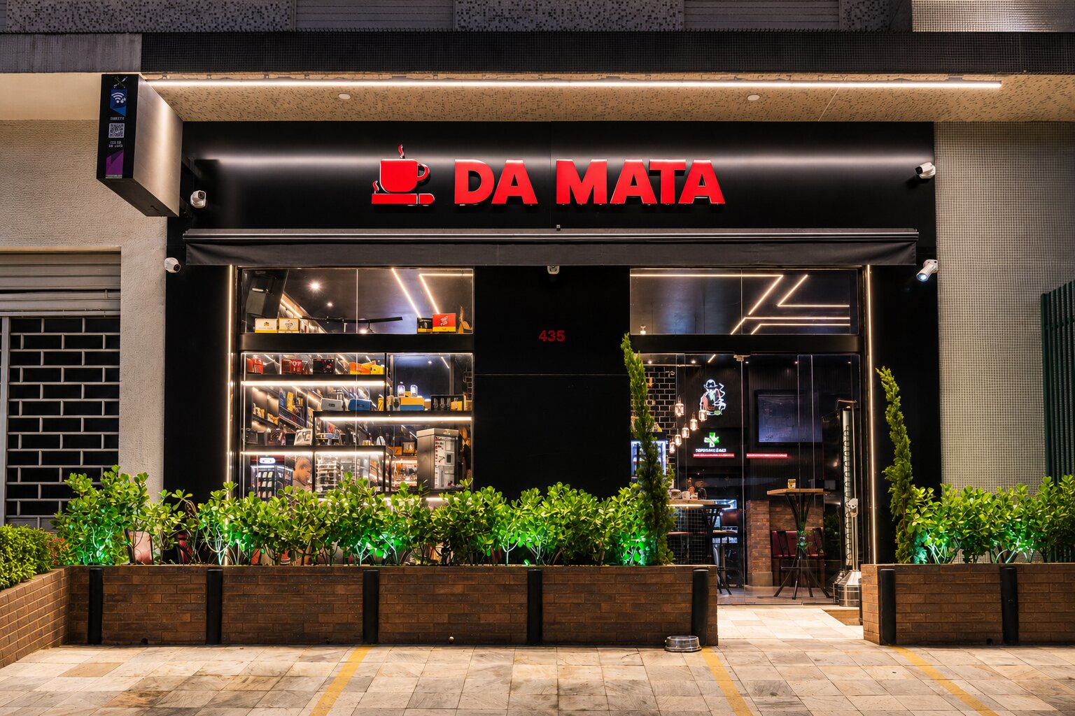 Fachada do café Da Mata com iluminação moderna e plantas.